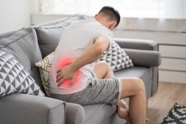 Un hombre con dolor de espalda sentado en el sofá.  