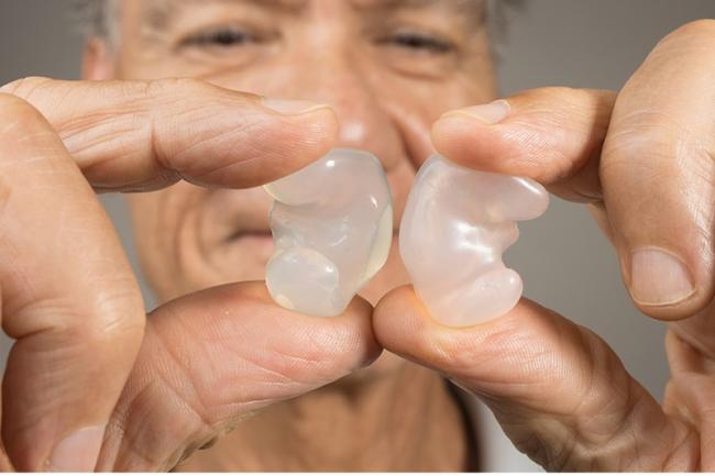 Imagen de un hombre mayor sosteniendo tapones transparentes para los oídos entre dos dedos.