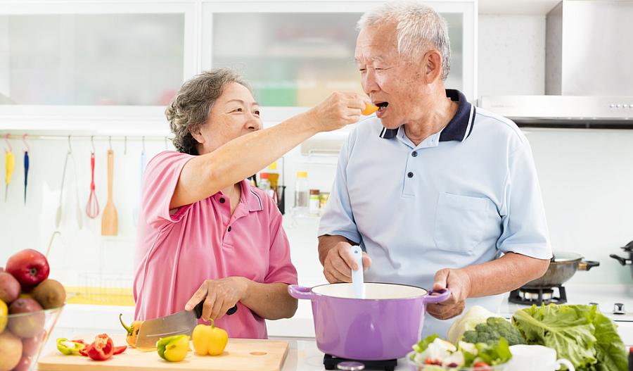 Foto de una pareja de adultos mayores cocinando verduras.
