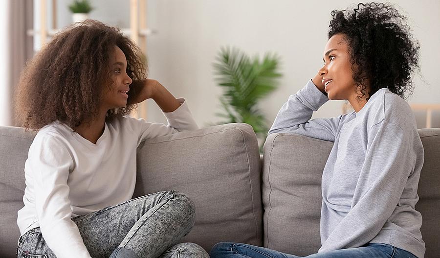 Foto de una madre escuchando a su hija adolescente mientras está sentada en el sofa