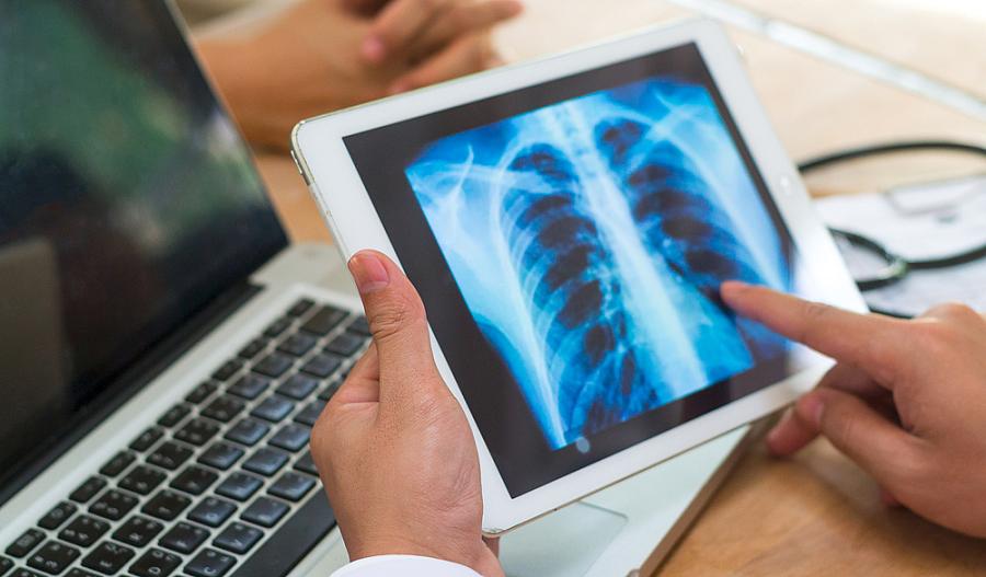 Foto de un proveedor de atención médica mirando una radiografía en su consultorio con un paciente.