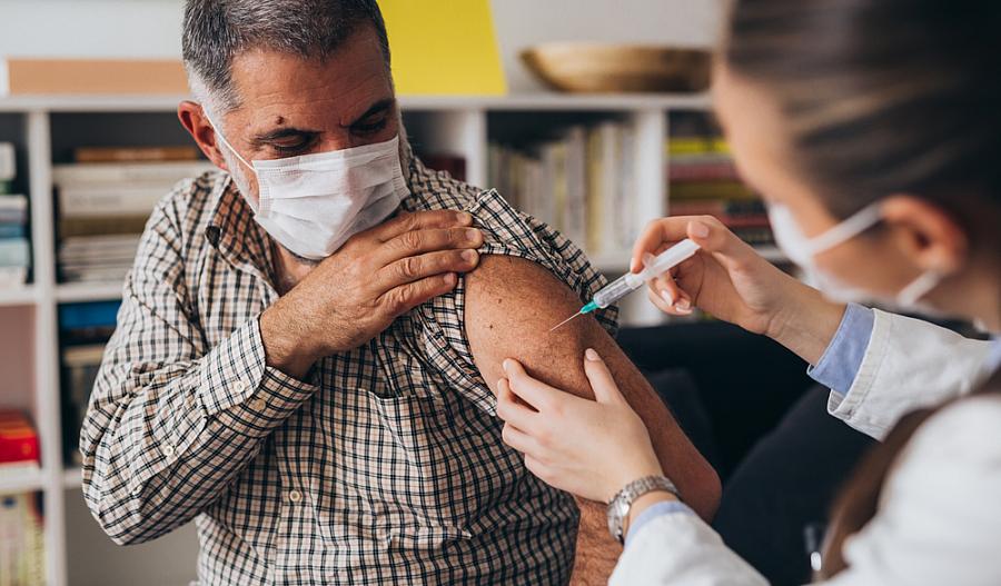 Foto de una persona con una máscara que recibe una vacuna COVID-19 de su proveedor de atención médica