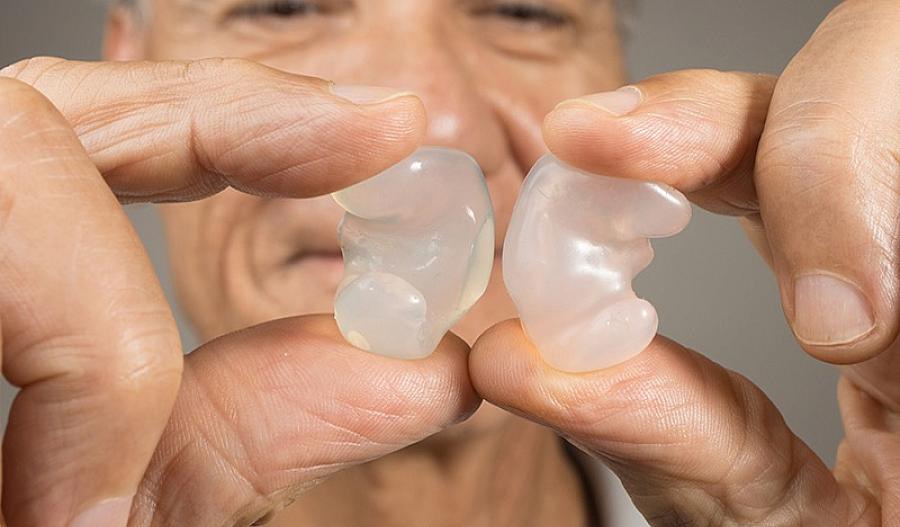 Imagen de un hombre mayor sosteniendo tapones transparentes para los oídos entre dos dedos.