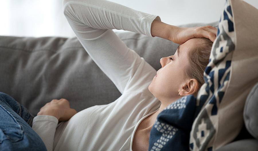 Una fotografía muestra a una mujer recostada en un sofá, con su mano en su frente, con los ojos cerrados, en actitud de sentirse mal.