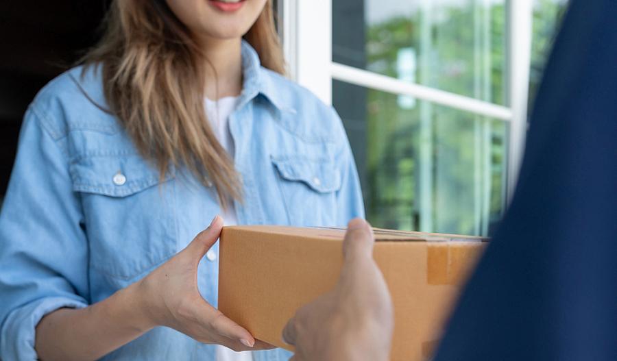 Fotografía de una mujer recibiendo un paquete de parte de un empleado de correos.